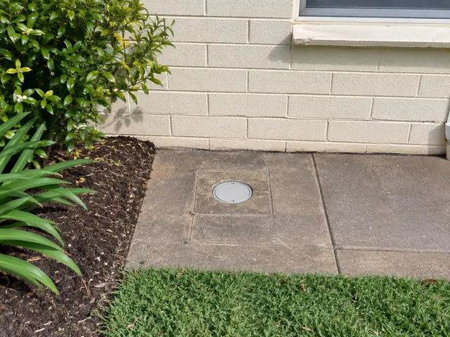 Capped access cover flush in paved area beside a brick wall and garden bed in Lalor Park